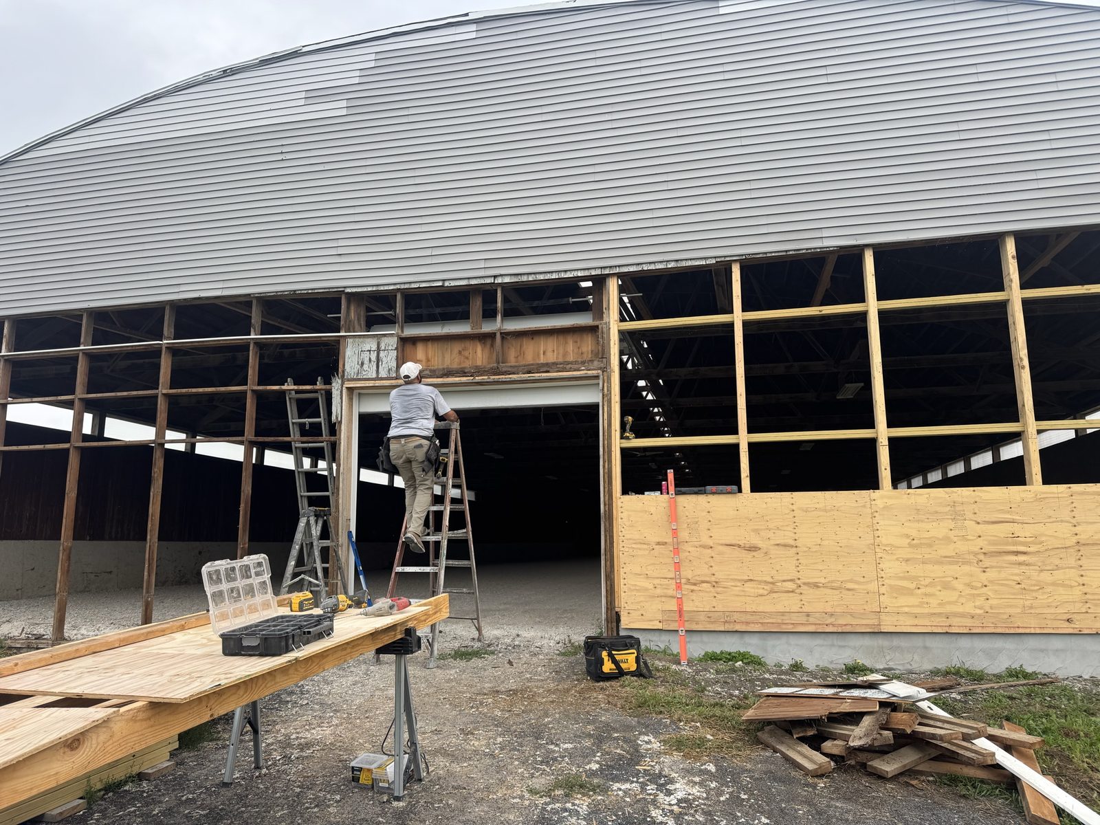 Barn gable end doorway showing old weathered header framing beside newly rebuilt stud walls and plywood sheathing