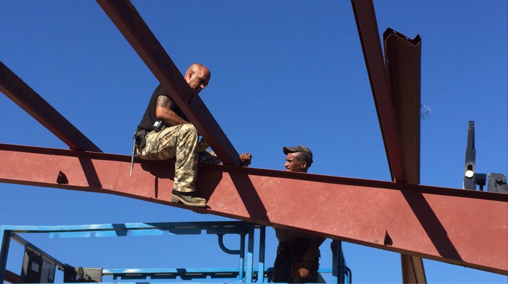 Two crew members working atop a steel beam against a clear blue sky