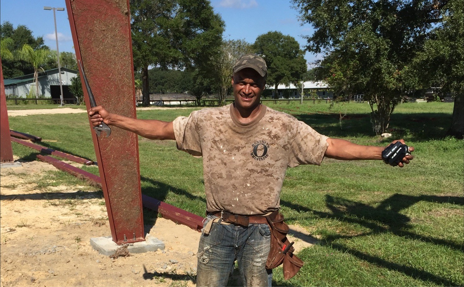 Crew member smiling next to a freshly set steel post at a barn construction site