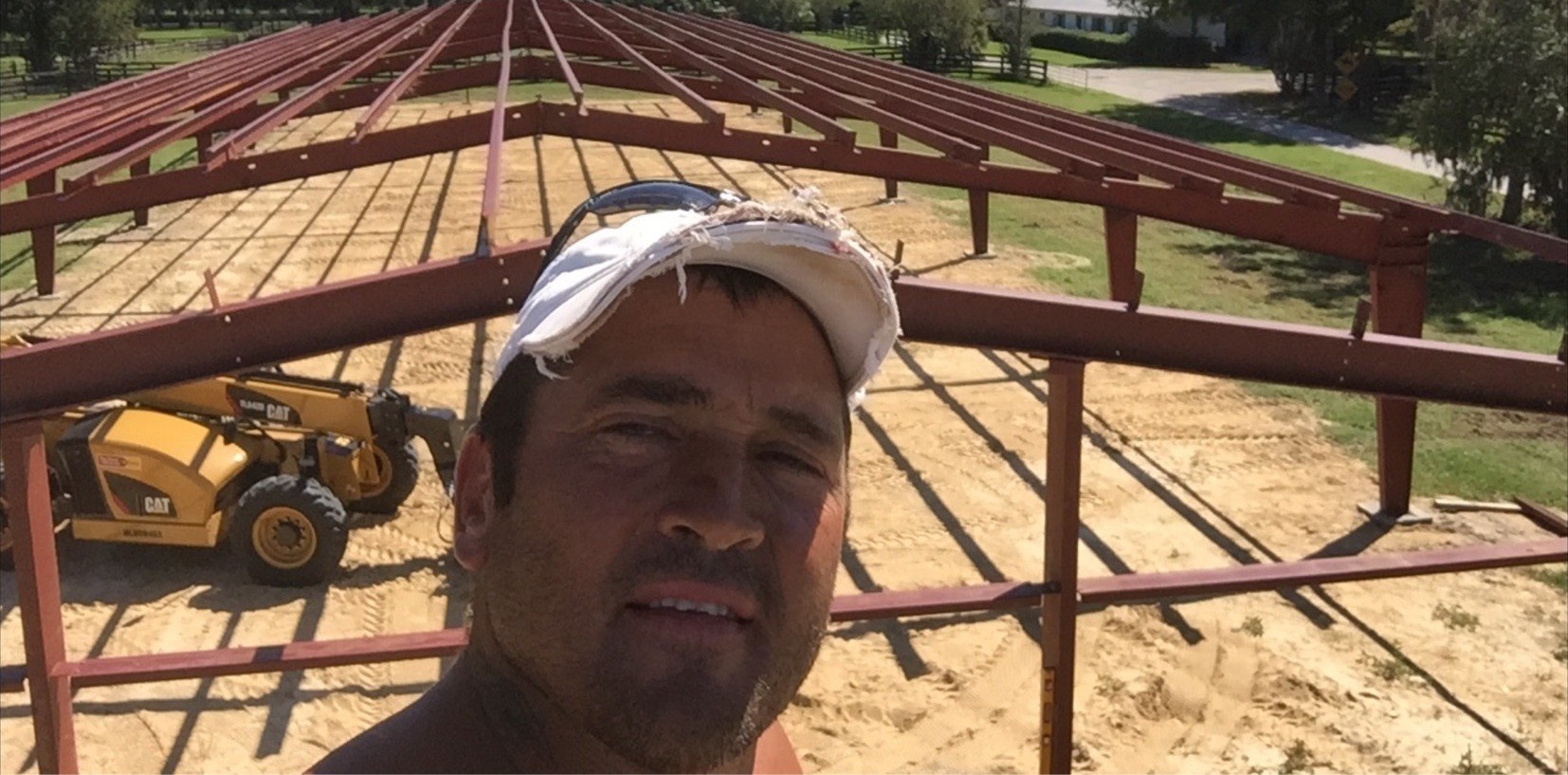 Crew member selfie in front of red steel trusses during a barn construction project