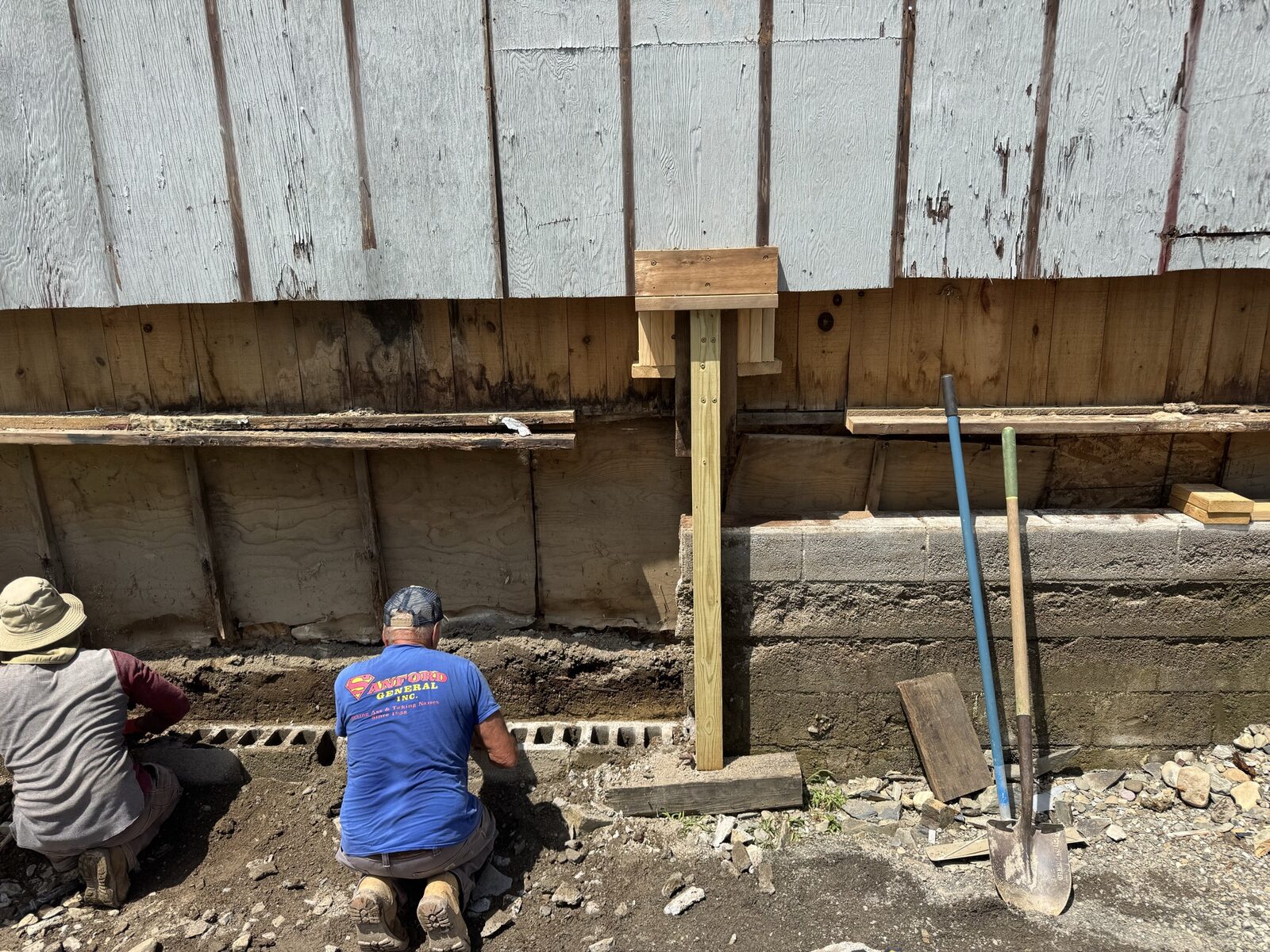 Two crew members repairing a sill and foundation area on an older home