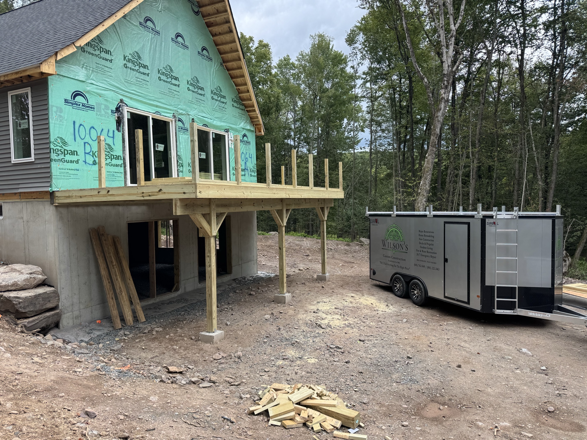 Elevated second-story deck framed on post supports at a new home under construction, with equipment trailer on site