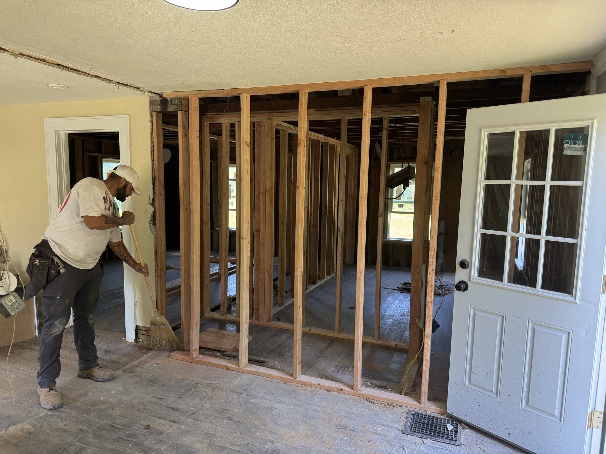 Crew member sweeping a freshly framed interior wall opening during a home renovation