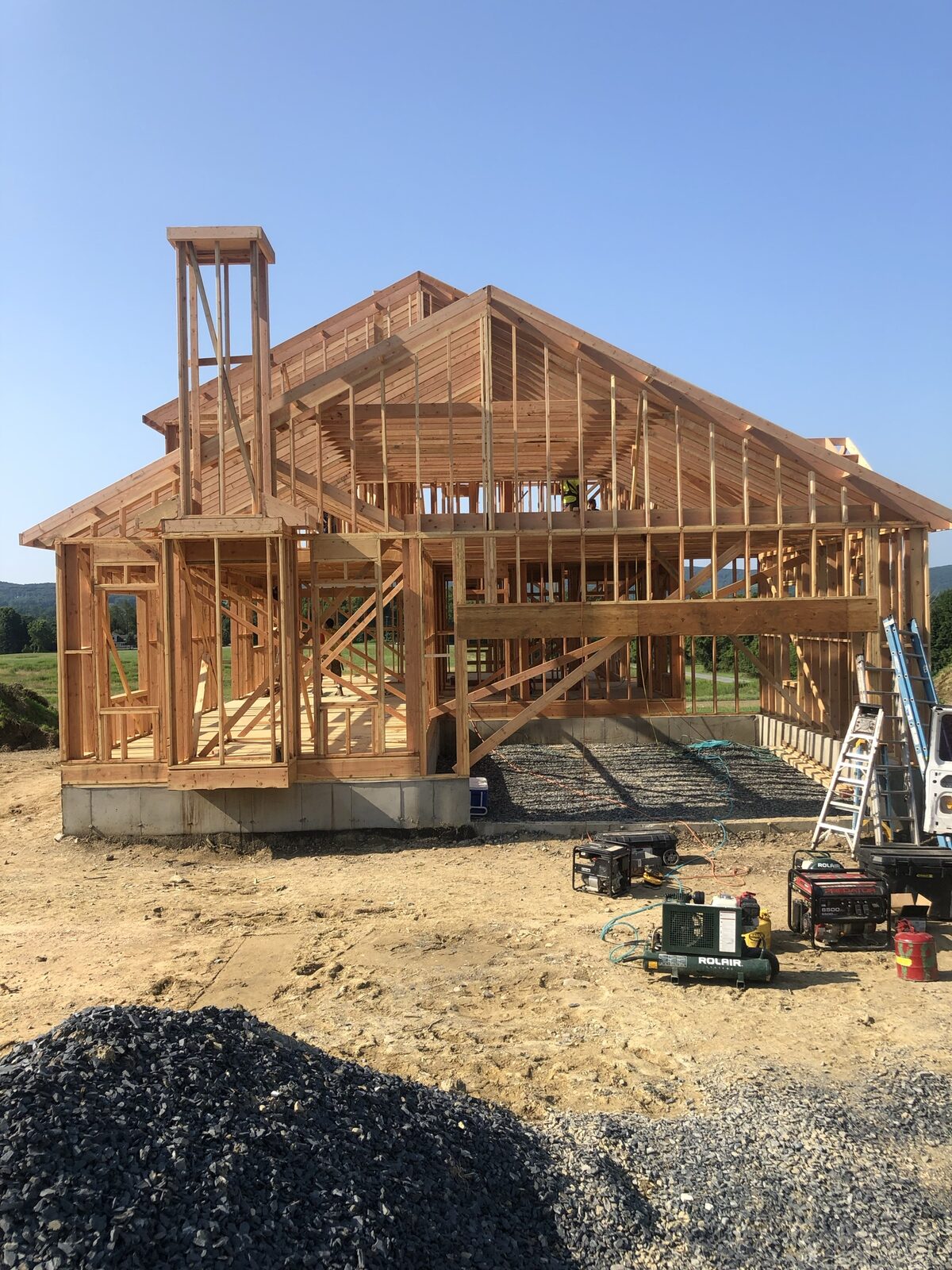 Fully framed custom home with complex roofline against a clear sky