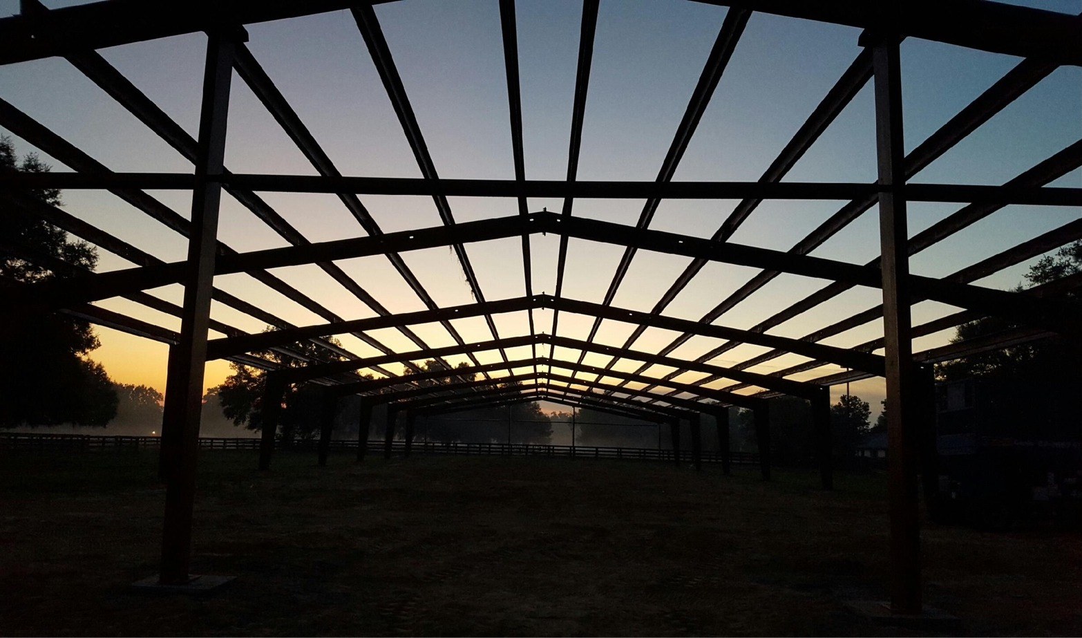 Silhouette of a large steel pole barn frame against a sunrise sky