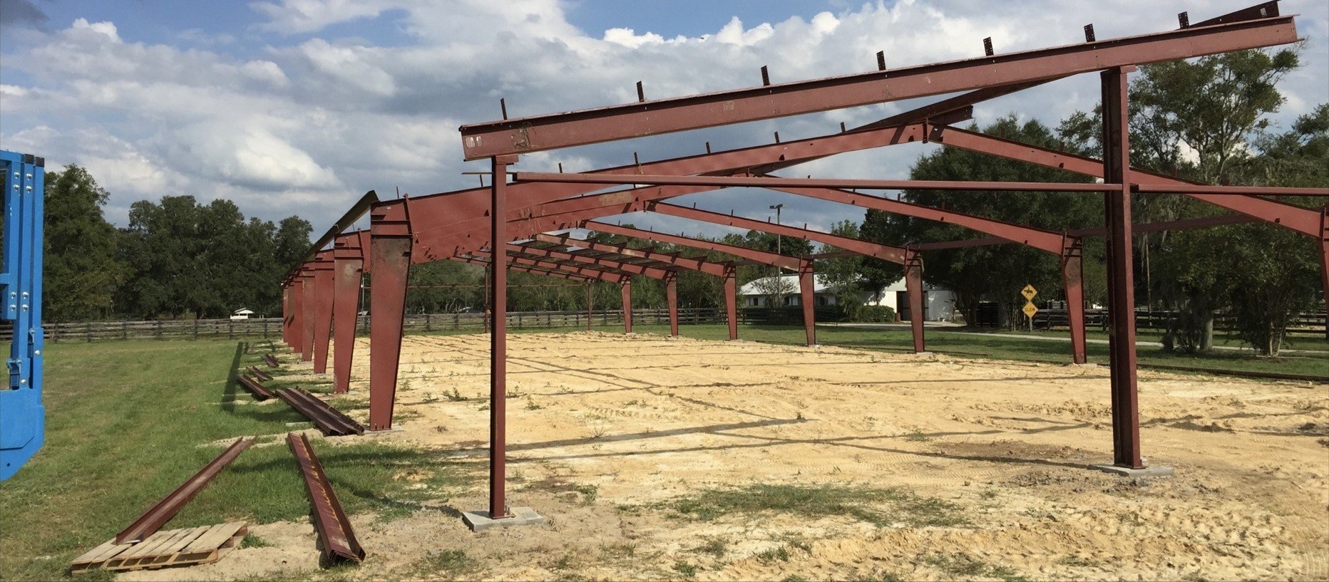 Wide view of a steel truss barn frame under construction with equipment trailer nearby