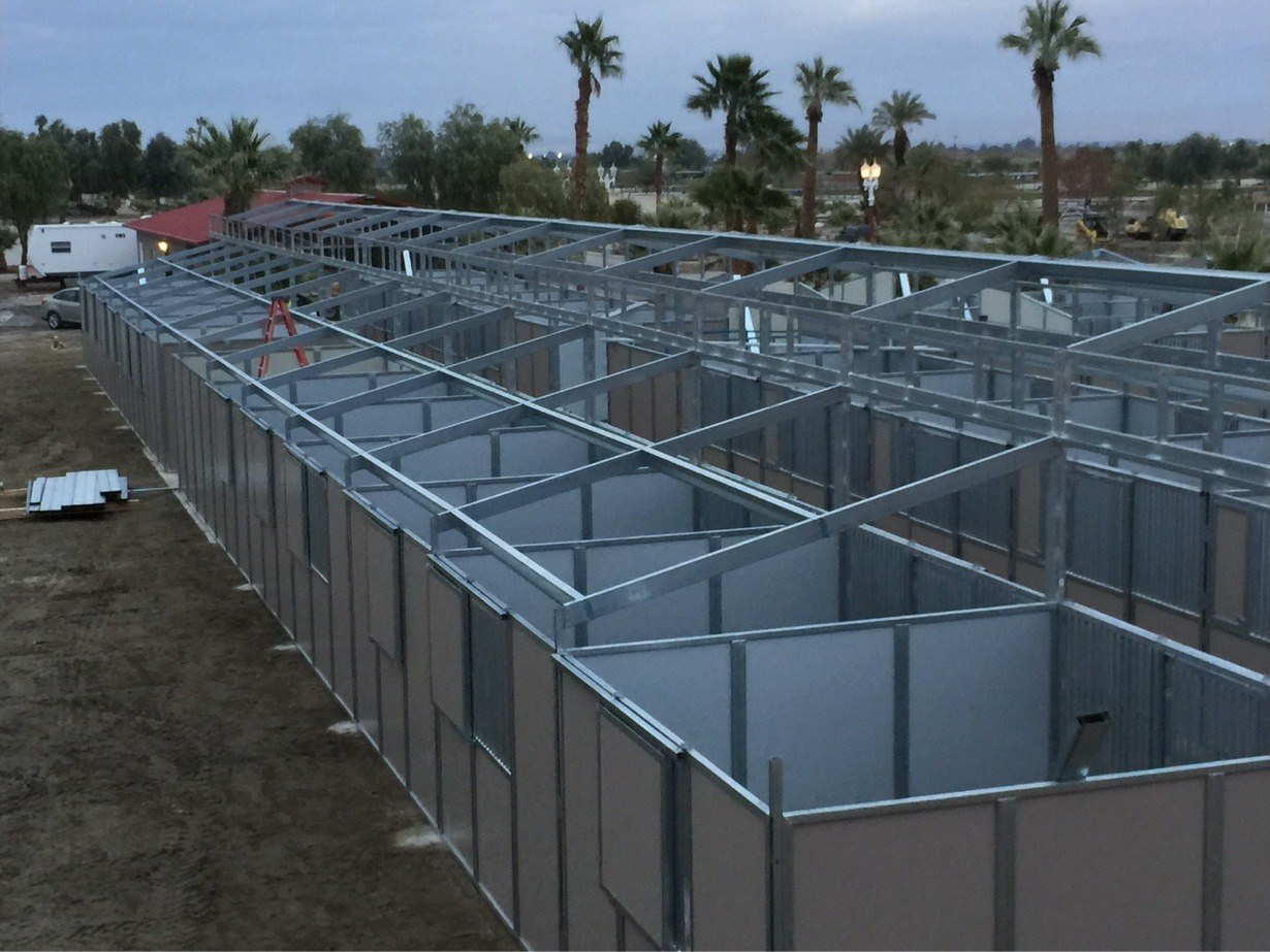 Aerial view of a large steel-framed warehouse structure under construction near palm trees